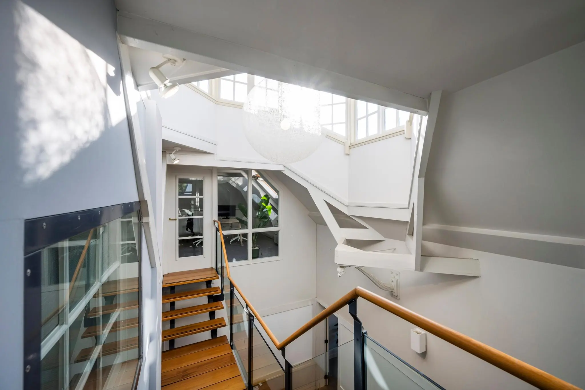 Licht trappenhuis met houten treden en een glazen balustrade in een woning aan de Prof. Tulpstraat.